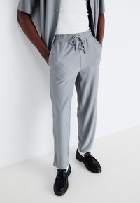 Grijze geribbelde broek met een elastische tailleband en een verstelbare trekkoord, gecombineerd met zwarte schoenen met een opvallend textuurontwerp.