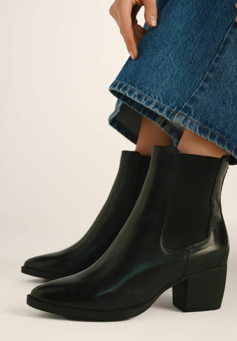 Czarne skórzane botki za kostkę z wąskim noskiem, elastycznymi bocznymi panelami i grubym obcasem, połączone z dżinsową spódnicą.