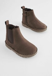 Stivaletti in suede marrone con punta arrotondata, pannelli laterali elasticizzati e zip. Presentano dettagli di cucitura a contrasto e una suola testurizzata.
