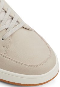 Beige Leder-Sneaker mit flachen Schnürsenkeln, strukturiertem Obermaterial und einer weißen Gummisohle mit einer Gummiaußensohle. Abgerundete Zehenpartie und subtile Nähdetails.