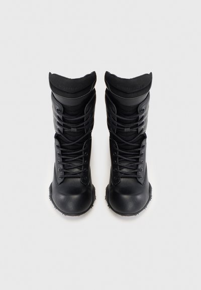 Bottes montantes noires en matériau synthétique. Elles présentent un design texturé avec des lacets, un col rembourré et une semelle en caoutchouc avec des crampons.