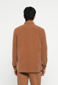 Brown corduroy shirt with a collared neckline, buttoned cuffs, and vertical ribbed texture. Visible stitching and a slightly curved hem.