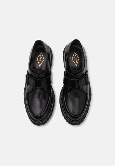 Pantofi din piele neagră cu vârful rotunjit, având o curea în față, talpă din cauciuc și un logo subtil în interior. Textură netedă, design minim.