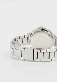 Stainless steel watch with a polished silver bracelet, round case, and visible crown; features a logo and a textured back.