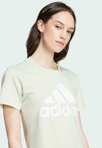 Camiseta de algodón de color verde claro con un gran logo de Adidas en blanco, cuello redondo clásico y mangas cortas, con una textura suave.