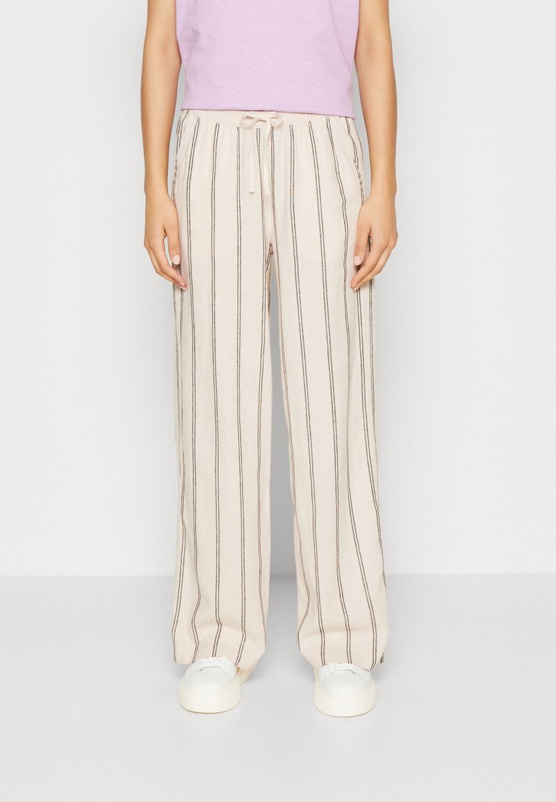 Beige, löst sittande linbyxor med vertikala ränder i brunt och accentfärger. Dragsko i midjan och sidofickor. Bärs tillsammans med vita sneakers.