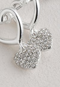 Pendientes en forma de corazón de tono plateado con piedras de imitación claras, que presentan un acabado liso y brillante y un brillo texturizado en los colgantes en forma de corazón.
