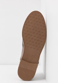 Semelle en caoutchouc marron d'une chaussure avec un motif texturé, portant la marque "ANNA FIELD" et la taille "37" embossées sur la surface.