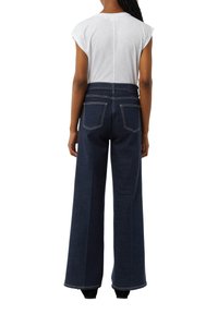 Donkerblauwe wijde denim jeans met een hoge taille, achterzakken en contrasterende stiksels. Gecombineerd met een wit topje.