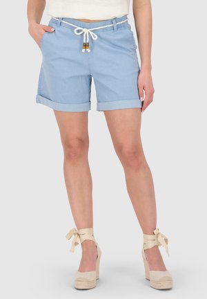 Frau trägt hellblaue Shorts mit umgeschlagenem Saum, einem weißen Seilgürtel und beigefarbenen Keil-Espadrilles, die um die Knöchel gebunden sind.