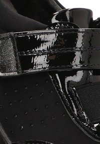 Scarpa sportiva nera con tomaia in vernice lucida, tessuto testurizzato con perforazioni e dettagli con cinturino regolabile in Velcro.