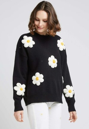 Pull noir en tricot avec des appliqués de marguerites blanches texturées et des centres jaunes, col rond et manches longues à côtes.
