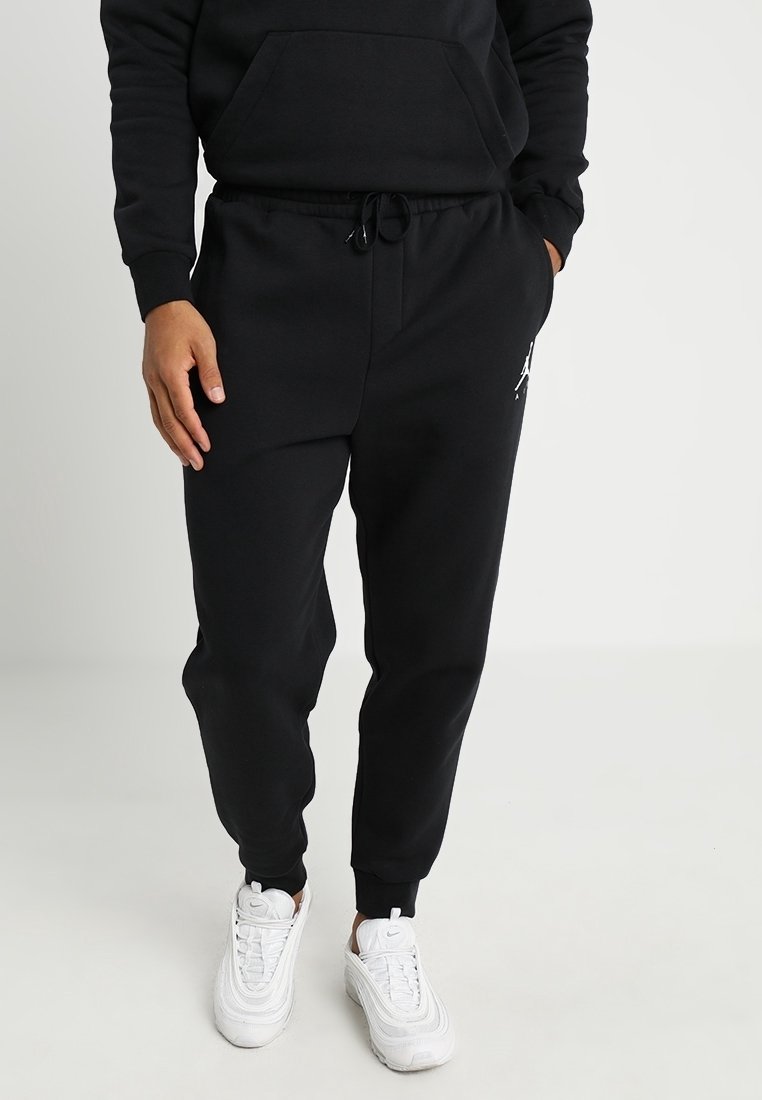 Černé tepláky s šňůrkou v pase a bočními kapsami, na levém stehně s bílým logem. Nosené s bílými teniskami.