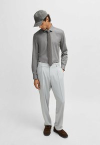 Graues Langarmhemd, gemusterte Krawatte, hellgraue Hose und graue M�ütze. Braune Slipper. Normale Passform, glatte Textur und klassisches Design.