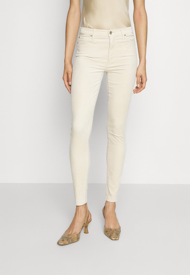 Jeans beige slim fit con una texture liscia, dotati di chiusura a bottone e tasche, abbinati a scarpe con tacco in pelle stampa serpente di colore marrone chiaro.