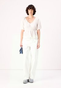 Haut blanc à manches courtes avec un tissu texturé, taille cintrée. Pantalons blancs amples, associés à des chaussures grises et un sac à main bleu.