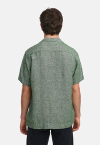 Camicia verde a maniche corte realizzata in tessuto strutturato, caratterizzata da un taglio dritto, colletto casual e un motivo sottile.