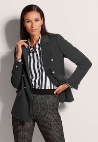 Dunkelgrauer, doppelt knopfseitiger Blazer mit silbernen Knöpfen, kombiniert mit einem schwarz-weißen gestreiften Hemd und strukturierten schwarz-weißen gemusterten Hosen.