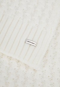 Sciarpa lavorata a maglia color bianco sporco con motivo a costine e texture liscia. Presenta una targhetta con il logo WITTCHEN in argento.