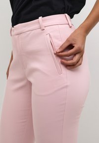 Light pink trousers with a smooth texture, featuring a zippered pocket on the side and a tailored fit at the waist.
