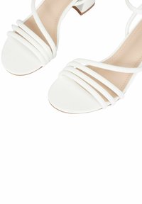 Sandali bianchi con cinturini, caratterizzati da più fasce orizzontali che attraversano il piede e un piccolo tacco a blocco con soletta color nudo. Finitura in materiale liscio.