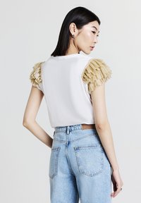 T-shirt bianca con maniche beige arricciate, abbinata a jeans in denim azzurro chiaro a vita alta con tasche posteriori e un'etichetta in pelle.