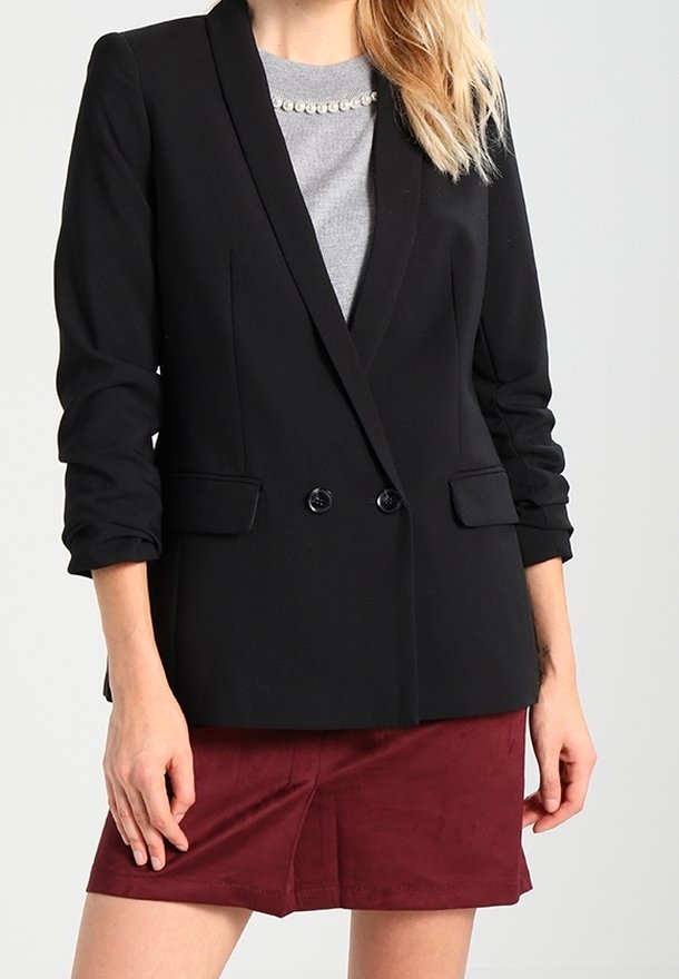 Blazer noir à la coupe ajustée, design croisé avec des revers crantés. Un haut gris en dessous, associé à une jupe bordeaux.