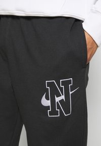 Svarta träningsbyxor i bomullsblandning, med en broderad vit "N"-logga och Nike-swoosh på sidan. Elastiskt midjeband med fickor.