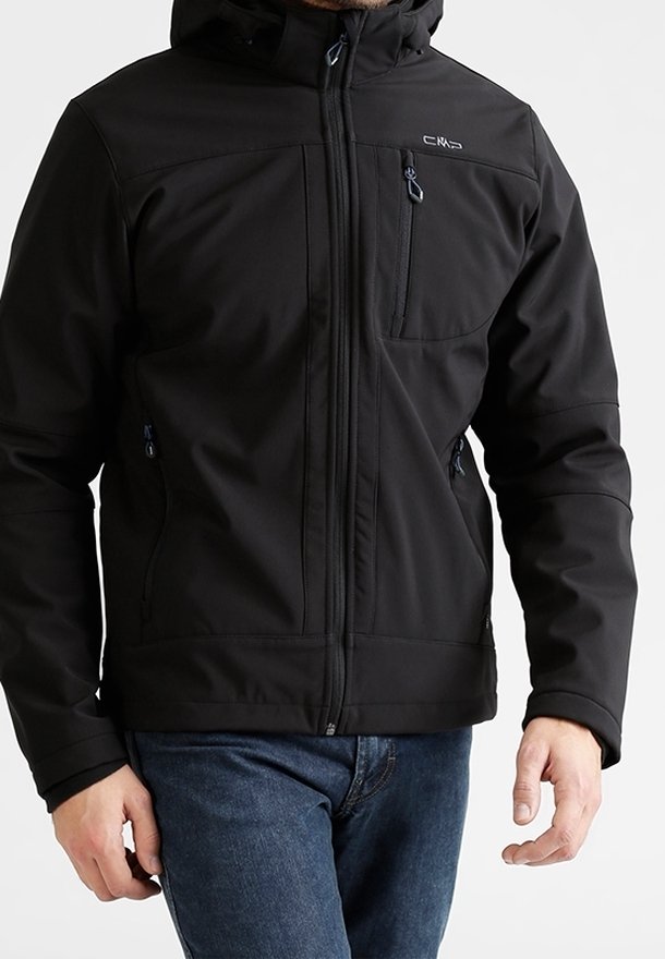 Homme portant une veste noire zippée avec capuche et poches zippées sur la poitrine et les côtés, associée à un jean bleu.