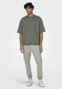 T-shirt gris oversize à encolure ronde, associée à un pantalon cargo gris clair avec poches latérales et bas élastiqués. Baskets blanches.