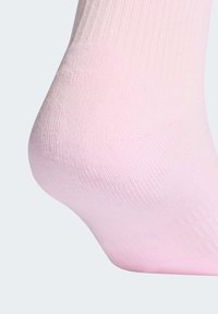 Jalutuskäsi, mis kannab heleroosat soonikutega sokki, rõhutades kanna ja pahkluu piirkonda, ühevärvilise tausta taustal.