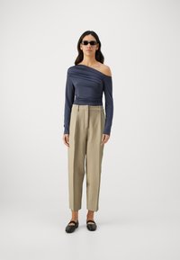Navy off-shoulder top with gathered texture, paired with light beige high-waisted trousers and black flat shoes. Model wearing sunglasses.