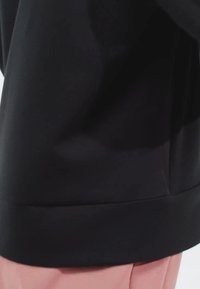 La felpa nera presenta un orlo arrotondato, un tessuto morbido e una vestibilità rilassata. I dettagli delle cuciture laterali sono visibili, migliorando il design complessivo.