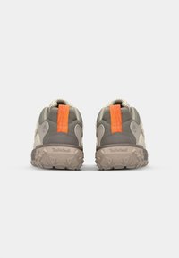 Graue und beige Sneaker mit strukturiertem Obermaterial, gepolstertem Kragen, orangefarbenem Fersenpanel und robustem Sohlenprofil mit multidirektionalen Rillen für optimale Bodenhaftung.