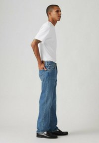 T-shirt bianco a maniche corte abbinato a jeans azzurri chiari. I jeans hanno una vestibilità dritta e cuciture in vista, indossati con mocassini neri.