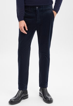 Marineblaue Cordhosen mit geradem Schnitt, ausgestattet mit einem Knopfverschluss und vorderen Taschen. Kombiniert mit schwarzen Leder-Stiefeletten.