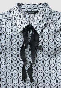 Kragenbluse mit einem sich wiederholenden kreisförmigen Muster in Schwarz, Grau und Hellblau, mit einem schwarzen Banddetail am Hals.