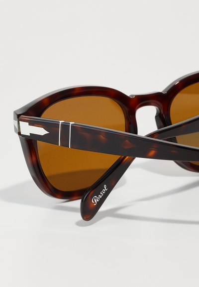 Barna teknős mintájú napszemüveg, szögletes kialakítással, barna lencsékkel és ezüst kiegészítőkkel a szárakon. A márkaneve "Persol" felirat található.