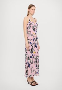 Rožinė maksi suknelė iš audinio su grafikiniu raštu, dekoruota juodais, mėlynais ir geltonais akcentais. Plonos petnešėlės ir laisvas siluetas.