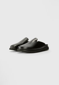 Crne kožne slip-on cipele s glatkom površinom, zaobljenim vrhom i teksturiranom gumom. Dizajn uključuje minimalistički izrez na vrhu.