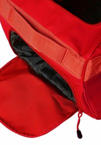 Bolsa de tela roja abierta con forro interior negro y cremallera, mostrando el compartimento principal y una correa tejida resistente en la parte superior.