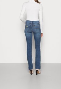 Blå denim flare jeans med midjehöjd, med bakfickor och en logopatch. Bärs med en åtsittande vit ribbad topp och klackar.