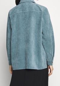 Giacca camicia in corduroy azzurro chiaro con colletto, polsini con bottoni e texture a coste verticali; presenta una vestibilità rilassata e un orlo dritto.