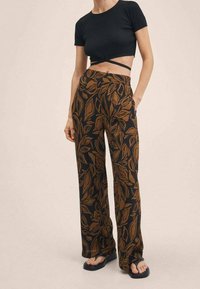 Zwarte geribbelde crop top, gecombineerd met wijde broek met een bladerenpatroon in bruin en donkerblauw. De outfit wordt aangevuld met eenvoudige sandalen.