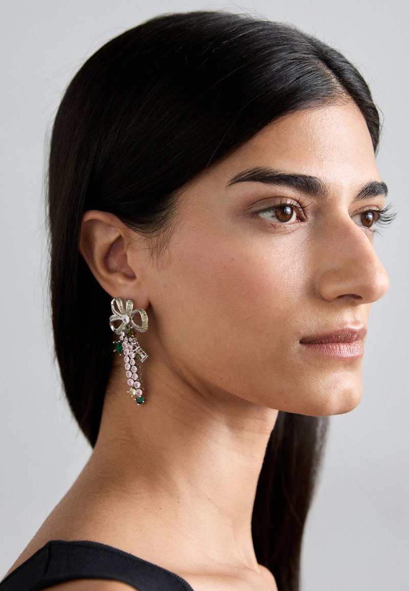 Silver floral earrings with a cascading drop, featuring pink and green stones and crystal accents, displayed on a model.