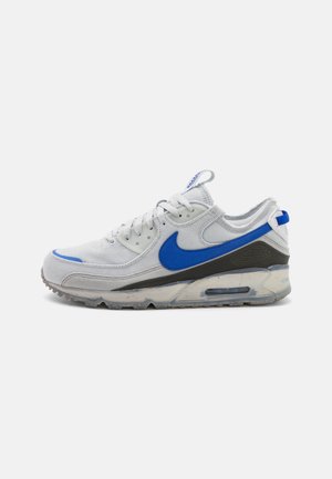 Biało-szary sneaker Nike Air Max z niebieskim logo Swoosh i akcentami, widoczną poduszką powietrzną w podeszwie oraz wiązaniem na sznurówki.