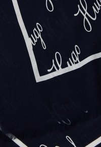Marine skjerf med hvit skrifttype mønster og kant, med frynser, laget av mykt stoff. Designet inkluderer gjentatte tekstdetaljer.