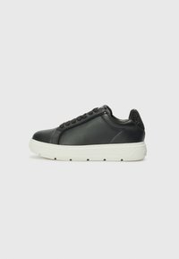 Zwarte leren sneaker met een witte rubberen zool, ronde neus, zes-ogige vetersluiting en een getextureerde hakaccent.