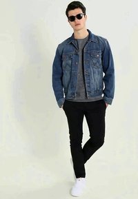 Denim jakna v svetlo modri barvi z oranžnim šivom, siva srajca, črne hlače in bele teniske. Sončna očala zaokrožujejo sproščen videz.