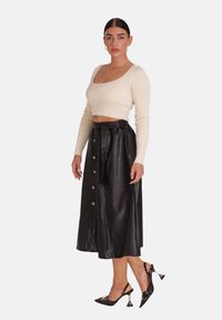 Top court en crêpe côtelé crème associé à une longue jupe en cuir noir avec des boutons sur le devant et une taille à nouer. Talons noirs avec des accents uniques.